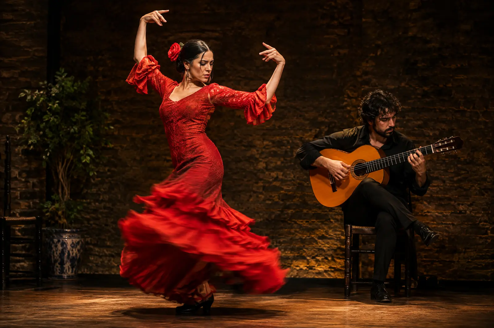 Flamenco dancer in a red ruffled dress mid-turn beside a seated guitarist